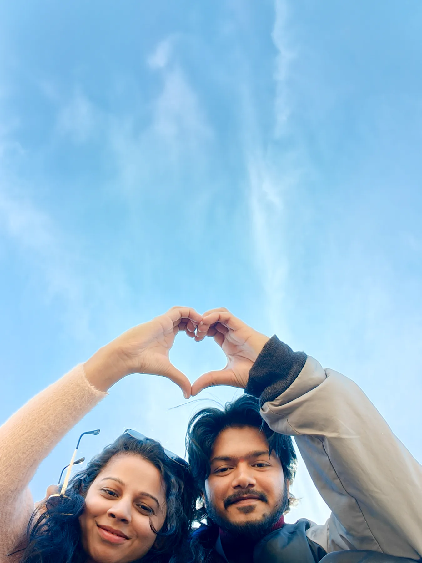 Pooja and Yuvaraj making a heart with their hands under a blue sky